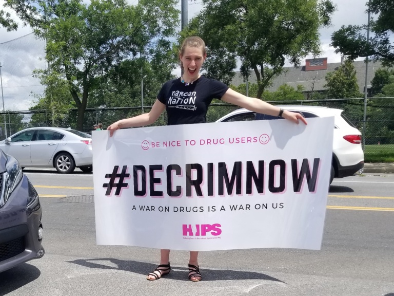 Alex from HIPS proudly presenting the banner "#DECRIMNOW". 2021. Photo by Laura Sislen.
